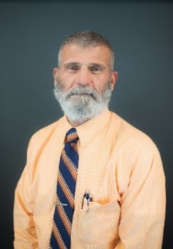 Photograph of a man with gray beard wearing dress shirt and tie. 